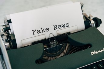 Schreibmaschine mit eingespanntem Blatt, auf dem Fake News geschrieben steht.