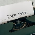 Schreibmaschine mit eingespanntem Blatt, auf dem Fake News geschrieben steht.